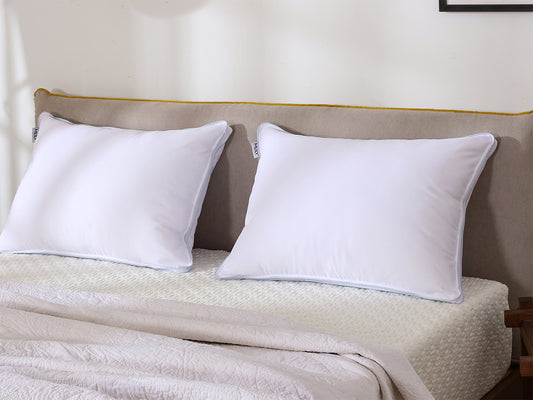 Two white Mlily pillows on a bed with a beige headboard.