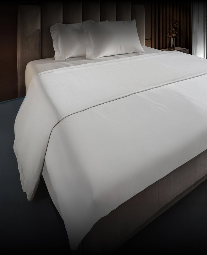 White bedspread on a Puffy mattress with a dark headboard in a dimly lit room