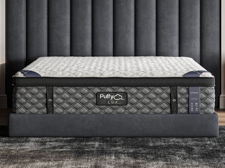 A hybrid mattress by Puffy Lux, shown in a bedroom setting, featuring a quilted pattern on the surface from Factory Direct Mattress KCK